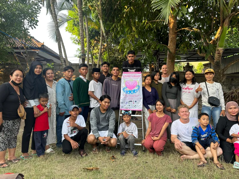 The community gathered in a Bali garden around a Community Assist basketball tournament poster.
